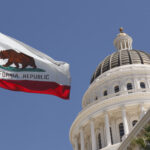 A bright blue sky with the California capitol dome and California flag waving in the breeze